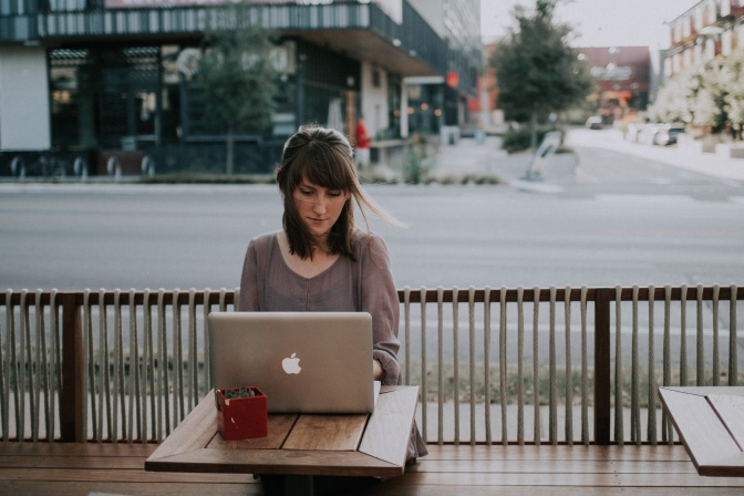 Eine Frau sitzt im Freien in einem Straßencafé und arbeitet an einem Laptop.