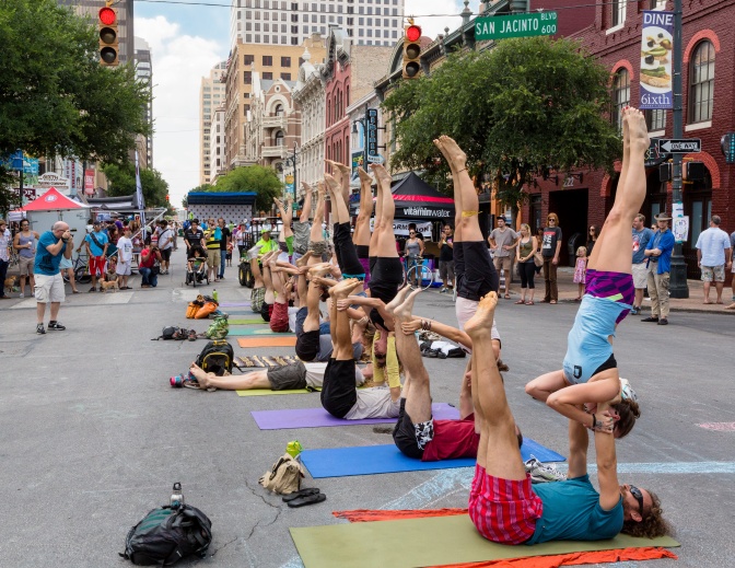 Eine Gruppe von Menschen macht im Freien, auf nebeneinander liegenden Yogamatten, gemeinsam Yoga.