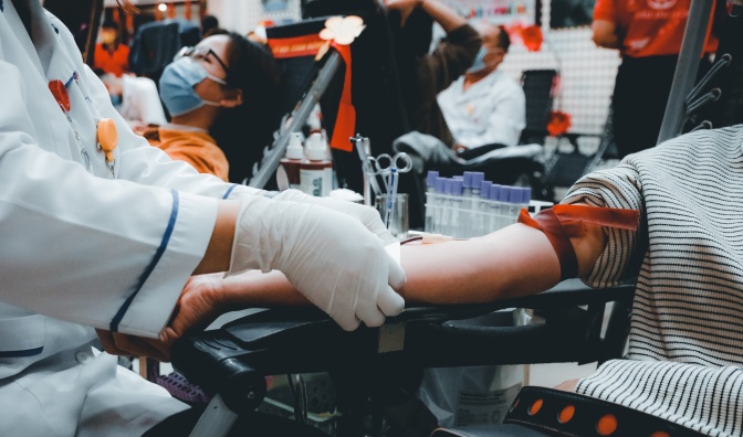 Der Arm eines Menschen, der gerade Blut spendet. Eine andere Person in weißem Kittel und mit Handschuhen nimmt das Blut ab.