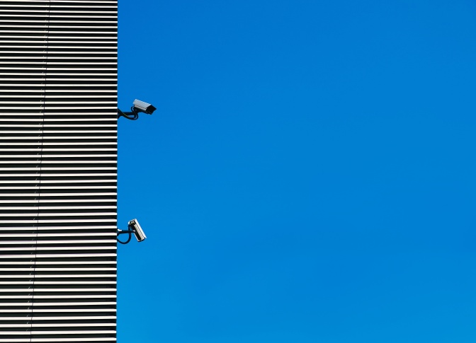 Zwei Überwachungskameras an einer Hauswand vor strahlend blauem Himmel