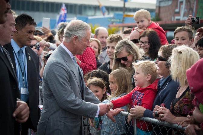 König Charles schüttelt Menschen hinter einem Metallzaun die Hand. Hinter ihm stehen Bodyguards.