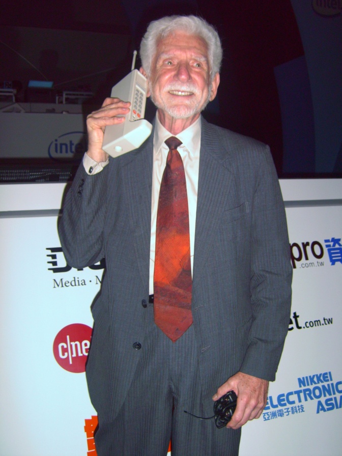Ein weißhaariger Mann im Anzug telefoniert mit einem großen, alten Mobiltelefon.