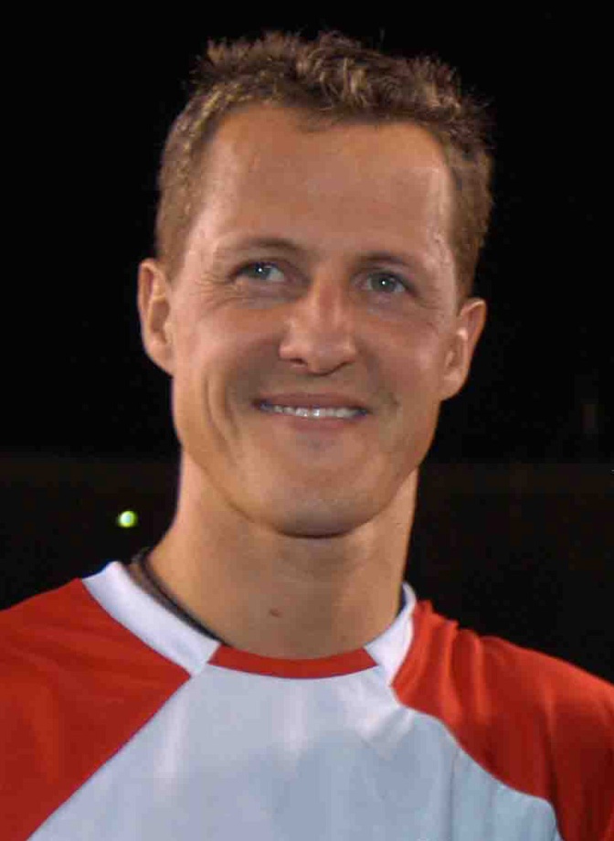 Michael Schumacher in einem rot-weißen Shirt und mit sehr kurzen Haaren. Er lächelt in die Kamera.