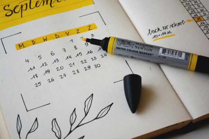 Ein gelber Stift liegt auf einem Kalender. Der Monat September ist aufgeschlagen. Einzelne Termine sind in dem Kalender markiert.
