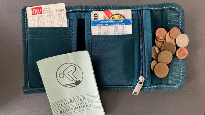 Ein geöffnetes Kinderportemonnaie mit Kleingeld, verschiedenen Dokumenten und einem Schwimmausweis.