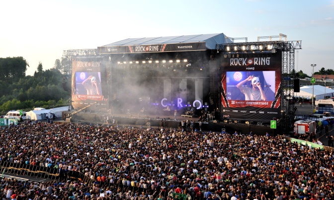 Eine große Bühne, vor der tausende Zuhörer*innen stehen. Bro wird rechts und links der Bühne auf große Leinwände übertragen.
