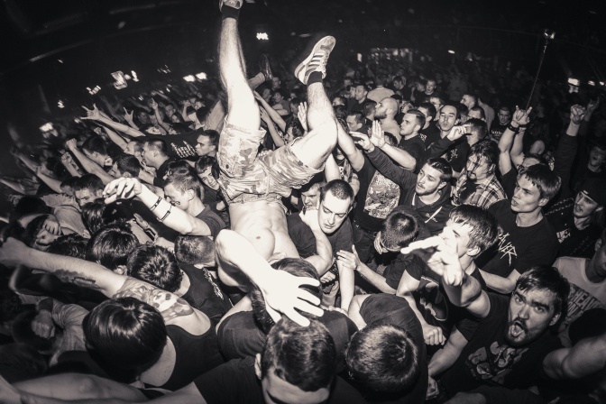 Schwarz-weiß Foto von wild tanzenden Menschen bei einem Konzert. Ein Mann mit freiem Oberkörper wird von der Menge in die Luft gehoben.