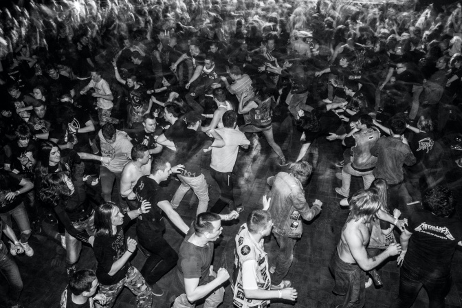 Schwarz-weiß-Foto einer wild tanzenden Menge. An der Kleidung der Menschen ist erkennbar, dass sie Metal-Fans sind.