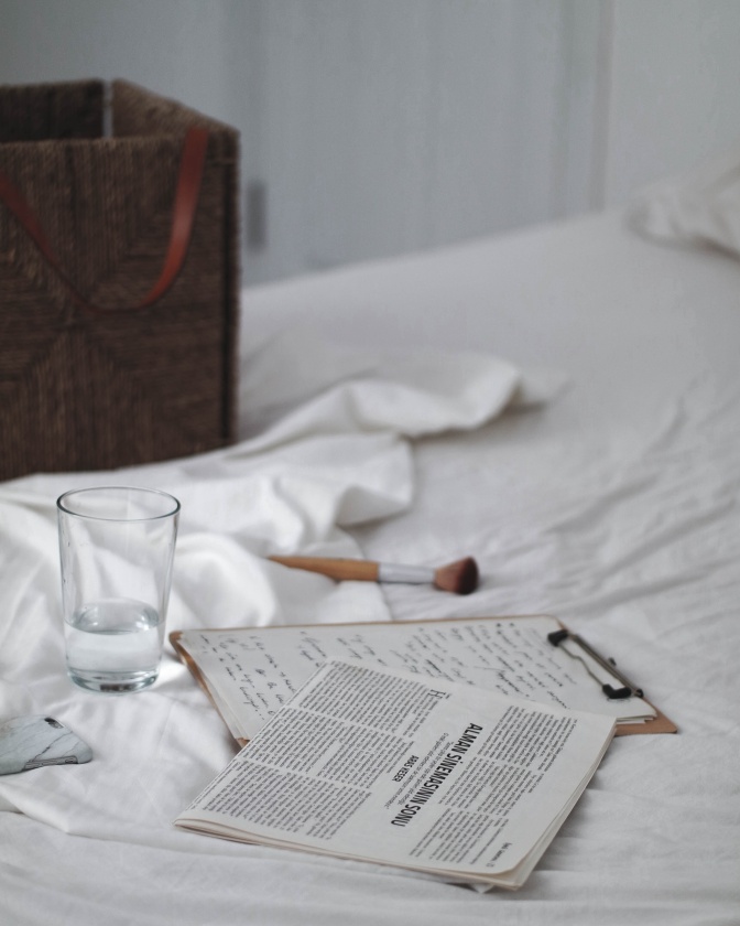 Ein handgeschriebener Zettel liegt neben einer Zeitung auf einem ungemachten Bett