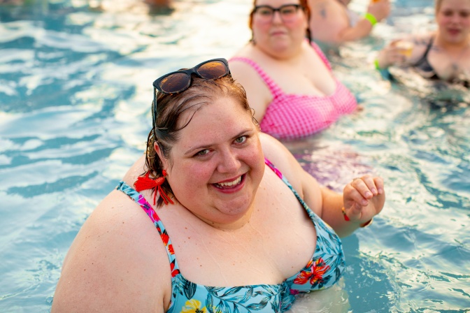 Mehrere dicke Frauen im Bikini in einem Schwimmbecken. Eine blonde Frau lächelt in die Kamera.
