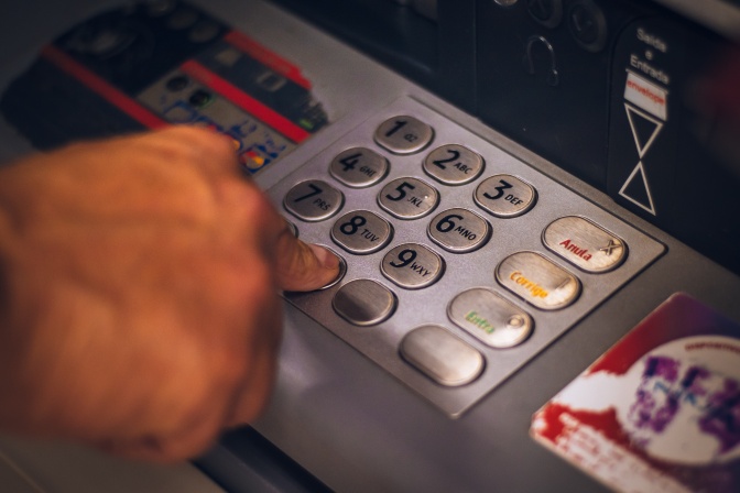 Eine Hand gibt Zahlen an der Tastatur eines Geldautomaten ein