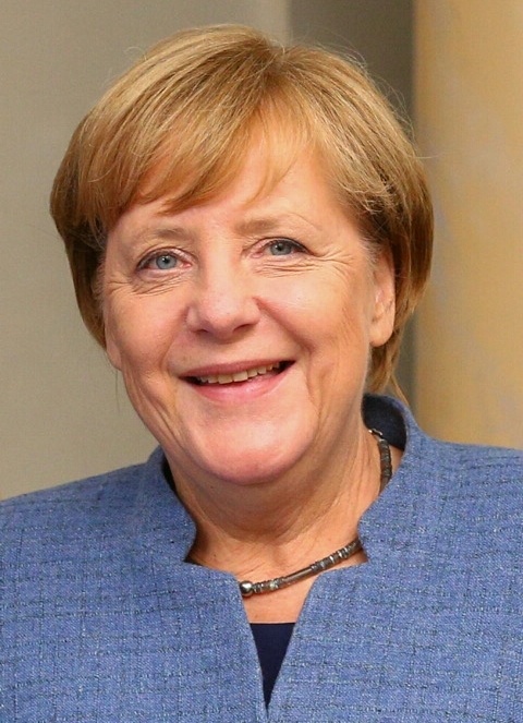 Angela Merkel in einem hellblauen Blazer mit kurzen blonden Haaren. Sie lächelt in die Kamera.
