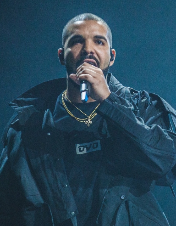 Drake in einem schwarzen Outfit auf der Bühne: Er singt in ein Mikro.