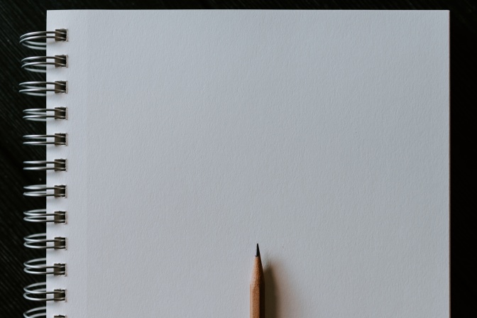 Ein Ringbuch mit leeren, weilen Seiten, darauf liegt ein Bleistift.