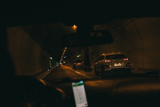 Eine Person fährt im Dunkeln mit dem Auto. Eine Navigation ist am Handy geöffnet.
