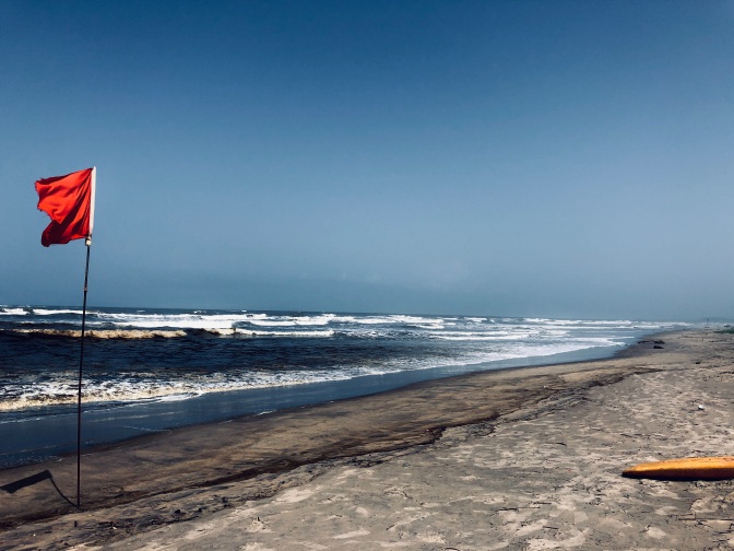 Eine rote Flagge steckt am Strand im Sand und weht im Wind.