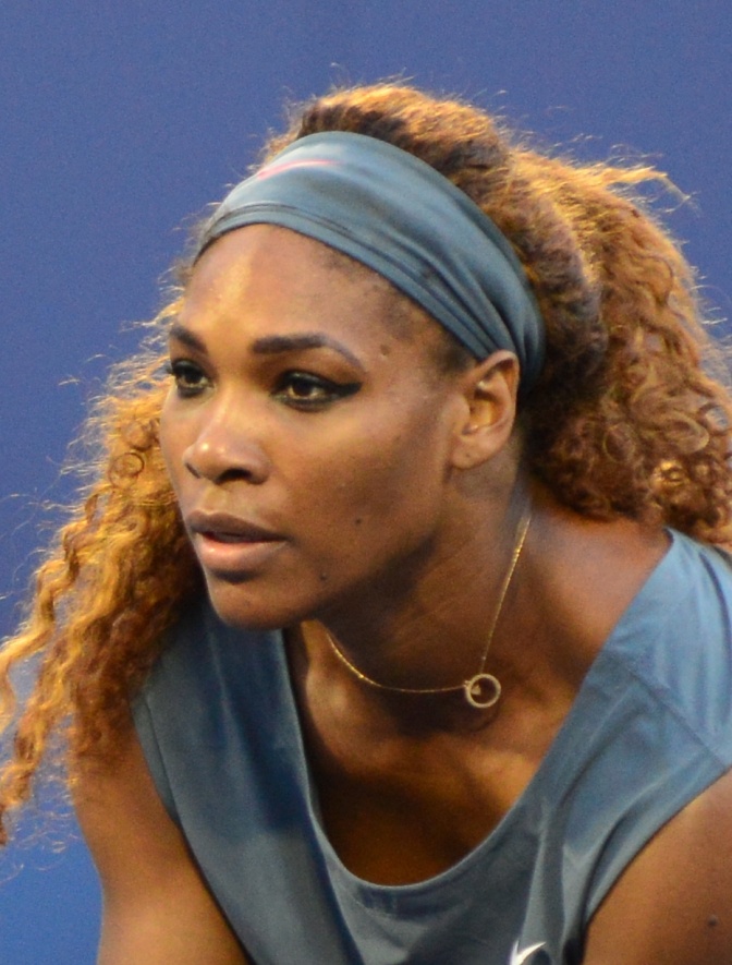 Serena Williams mit Shirt und Stirnband in hellblau. Sie hat braune lange gelockte Haare