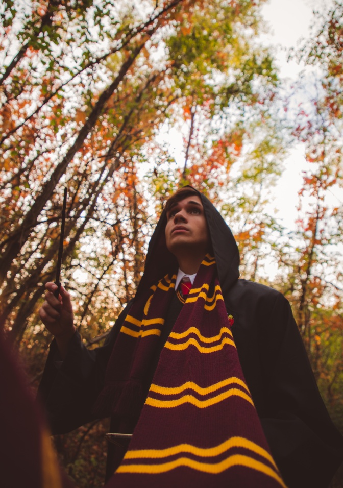 Ein als Harry Potter verkleideter Mann. er trägt einen langen Umhang mit Kapuze und einen Schal in den Farben gelb und rot.