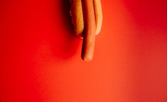 Eine Bockwurst im Brötchen auf rotem Hintergrund.