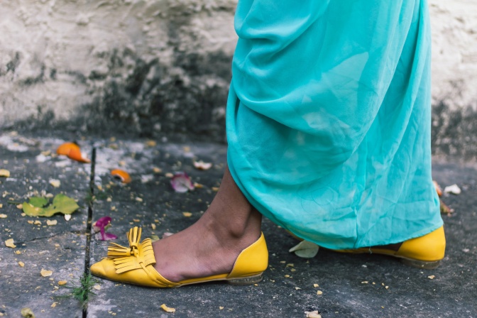 Füße und Beine einer Frau in türkisfarbenem Kleid mit gelben, flachen Sommerschuhen