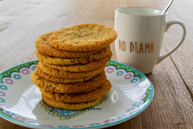 Ein Stapel großer, flacher Kekse auf einem Teller. Daneben steht eine Tasse mit dem Aufdruck: No Drama.