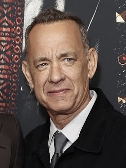 Tom Hanks mit sehr kurz rasierten Haaren in Anzug und Krawatte. Sein Gesicht ist schmal und faltig.
