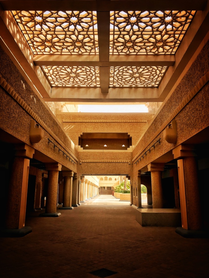 Ein Gang im Innenhof eines Riads, die Decke ist luftdurchlässig und mit Ornamenten gestaltet.