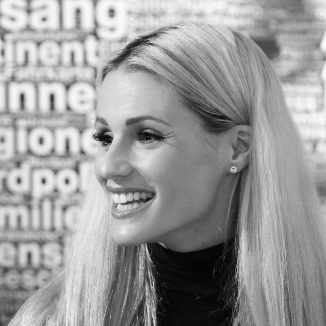 Schwazr-weiß-Foto von Michelle Hunziker mit langen, glatten blonden Haaren. Sie lächelt und wurde im Profil fotografiert.