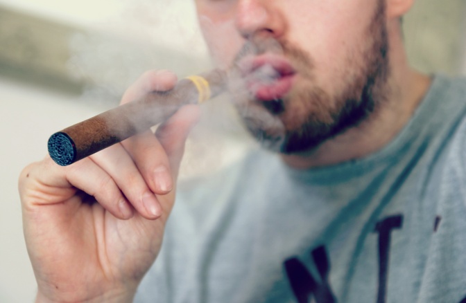 Ein Mann hat eine breite E-Zigarette in der Hand und stößt Rauch durch den Mund aus.