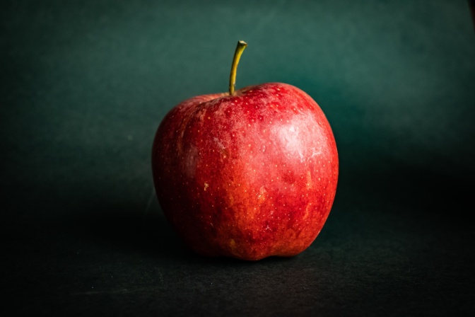 Ein glänzender, roter Apfel vor dunklem Hintergrund.