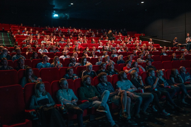 Viele Menschen sitzen in roten Samtsesseln im Kino.