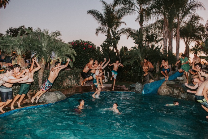 Menschen feiern eine Poolparty. Einige von ihnen springen vom Rand aus ins Wasser.