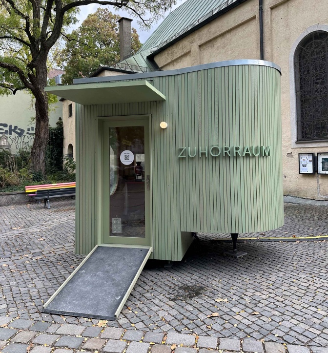 Ein grün gestrichener Wagen, an dem Zuhörerraum steht. Der Eingang ist über eine Weiche erreichbar.