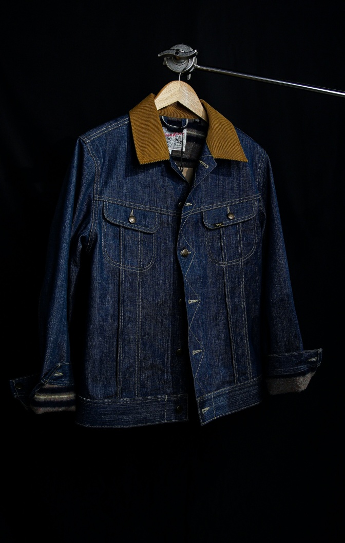 Eine Jeansjacke mit braunem Leder am Kragen hängt an einem Kleiderbügel.