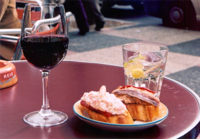 Ein Teller mit 2 Scheiben Baguette mit Schinken und Fisch, daneben steht ein Glas Rotwein.