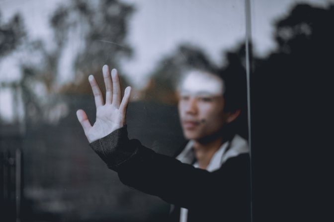 Ein junger Mann steht hinter einer Glasscheibe und drückt seine Hand dagegen.