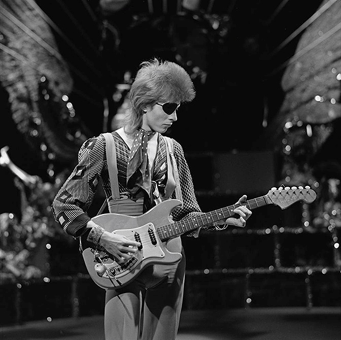 Ein schwarz-weiß-Foto von David Bowie, Gitarre spielend auf der Bühne.