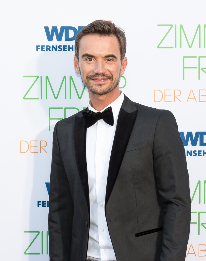 Florian Silbereisen in Anzug und mit Fliege vor einer Logowand der Sendung Zimmer frei