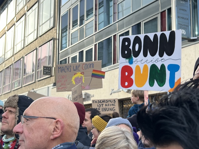 Demonstrant*innen mit Schildern stehen eng zusammen. Auf einem der Schilder steht: Bonn bleibt bunt.