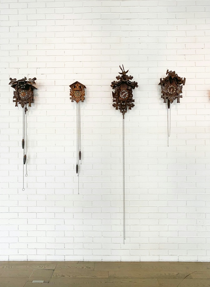 4 Kuckucksuhren hängen nebeneinander an einer weiß gekachelten Wand.