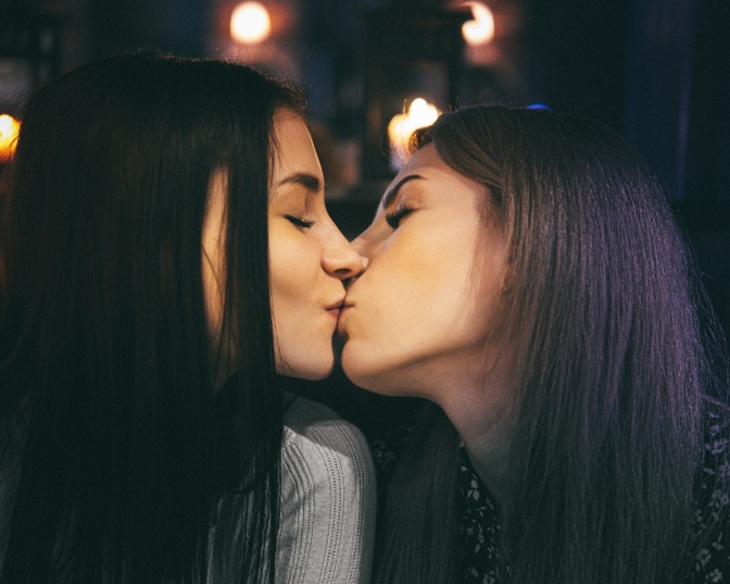 2 dunkelhaarige feminine Frauen küssen sich.