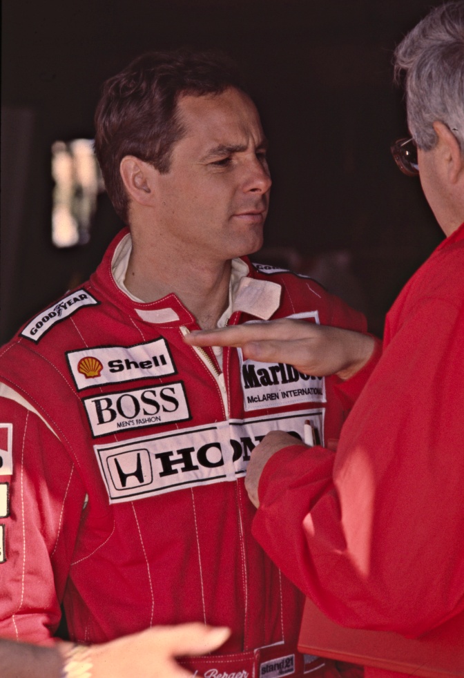 Gerhard Berger in einem roten Overall mit vielen Markenlogos.