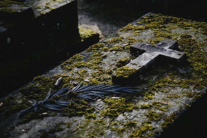Ein Grab mit einem Kreuz, die Grabplatte ist dick mit Moos bewachsen.