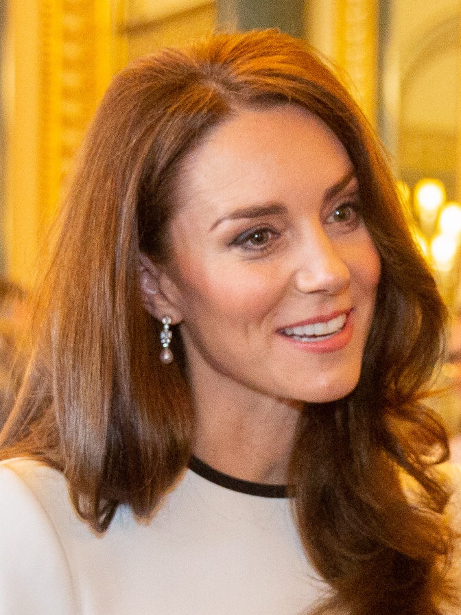 Prinzessin Kate mit leicht gewellten braunen Haaren in einem weißen Oberteil.