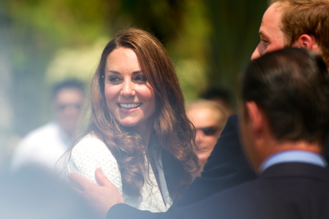 Prinzessin Kate dreht den Kopf seitlich und lächelt in die Kamera. Ihr Mann, Prinz William legt seine Hand auf ihren Arm.