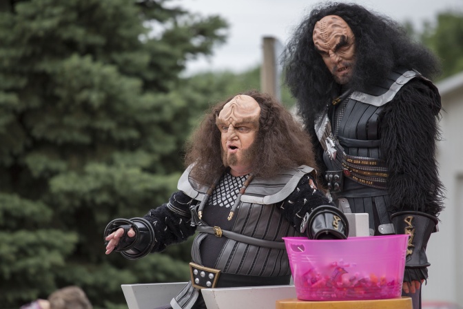 2 Schauspieler in Klingonen-Kostümen. Sie haben lange, dunkle Haare, Wülste auf der Stirn und tragen eine schwarze Uniform.