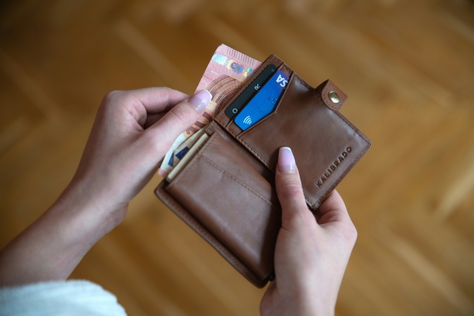 2 Hände halten einen geöffneten Geldbeutel in der Hand. Darin eine Geldkarte und ein 10-Euro-Schein.