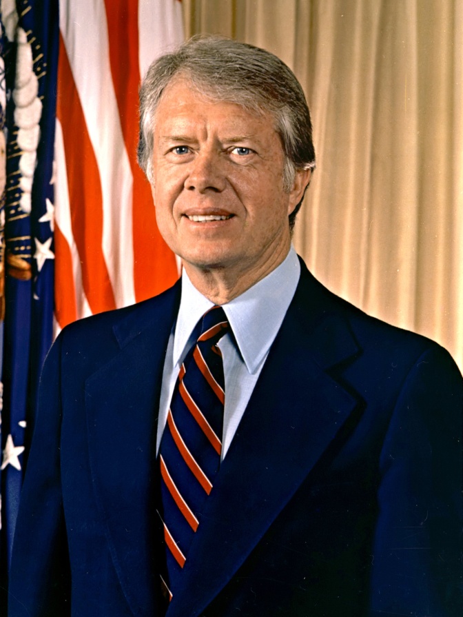 Jimmy Carter in Anzug und Krawatte vor der amerikanischen Flagge.