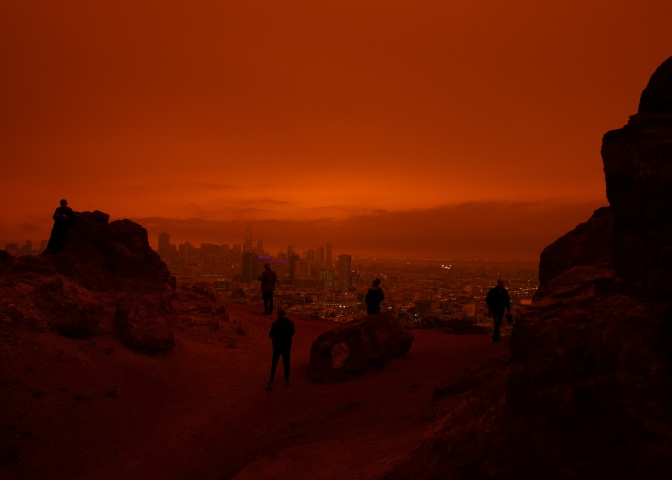 Mehrere Menschen in einer zerstörten Stadt. Man sieht nur ihre Umrisse und der Himmel ist feuerrot.