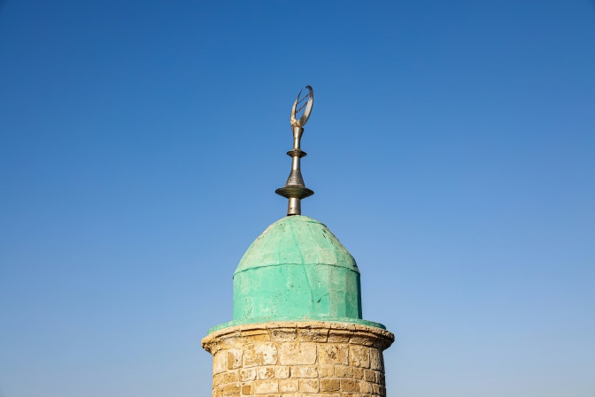 Ein Kuppeldach einer Moschee vor strahlend blauem Himmel. Oben auf dem Dach ist ei Halbmond aus Metall angebracht.